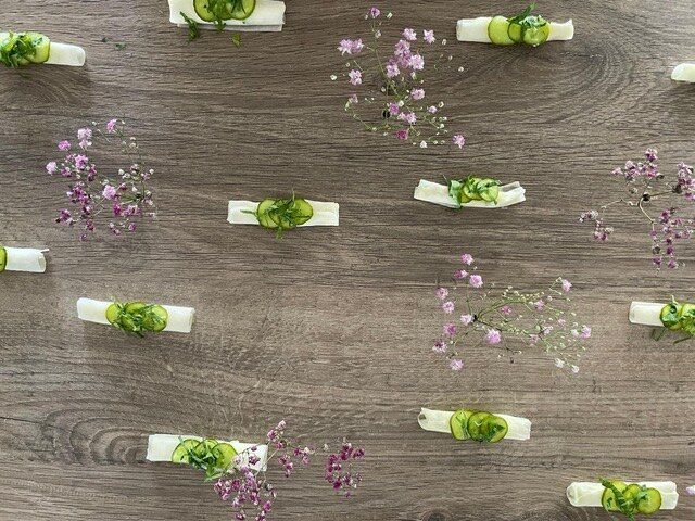 Amuse-Bouches mit Gurke und Kräutern, in Reihen auf Holz angerichtet, dazwischen kleine Blüten